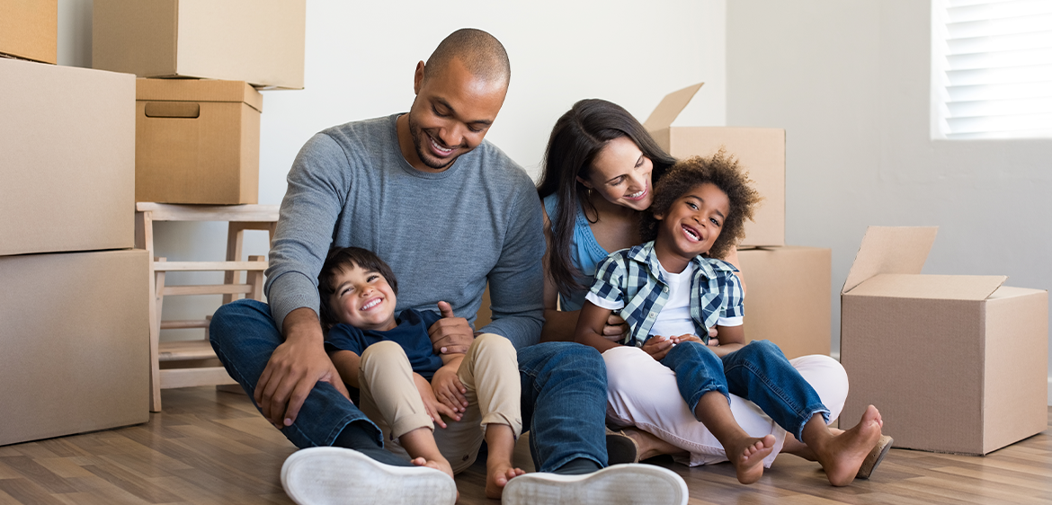 Happy family with two children having fun at new home. Young multiethnic parents with two sons in their new house with cardboard boxes.